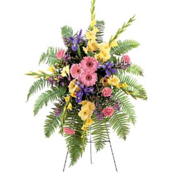 Tall standing spray with pink gerberas, yellow blooms and purple irises on a metal easel