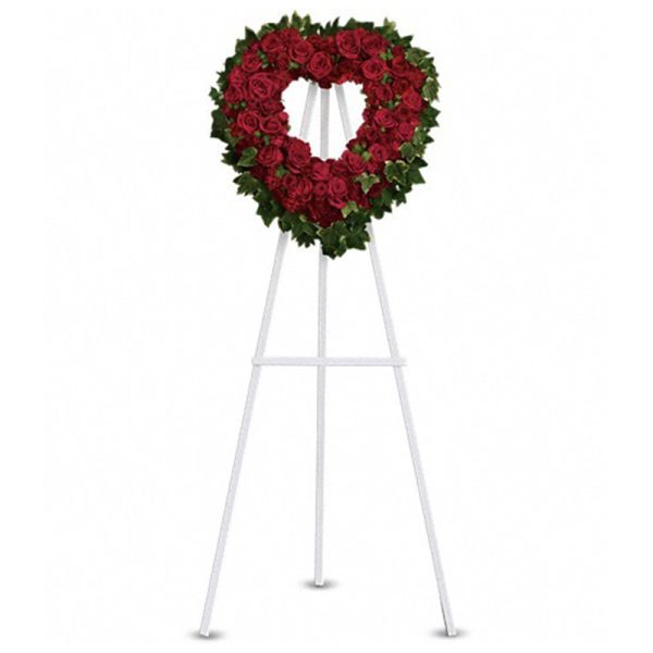 Heart-shaped wreath of red roses with greenery on a tall white easel stand
