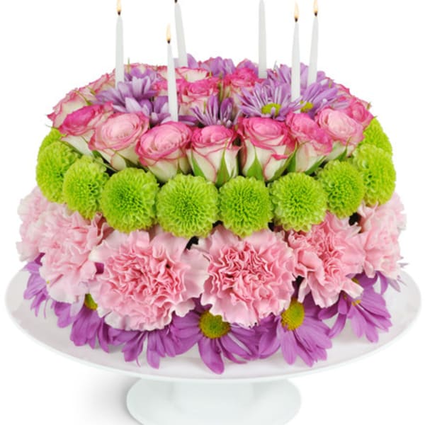 Round floral cake with pink and purple flowers and white candles