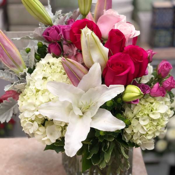 Bouquet of pink and white roses, lilies, and hydrangeas in a glass vase