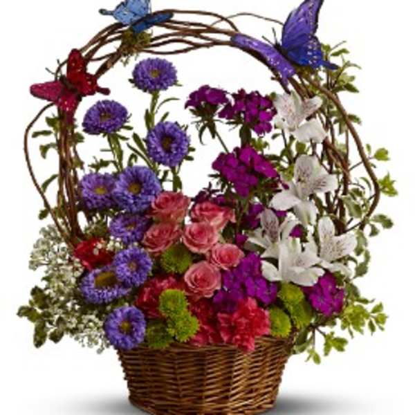 Basket arrangement of mixed pink, purple, and white flowers with butterflies on a vine arch