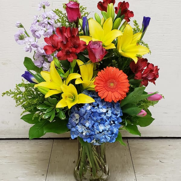 Colorful mixed bouquet in a clear glass vase with lilies, roses, hydrangea, and gerbera daisy