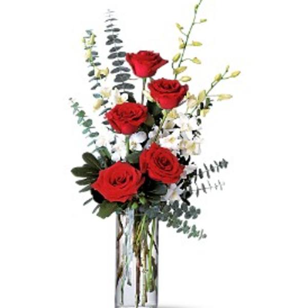 Red roses in a clear glass vase with white filler flowers and tall greenery