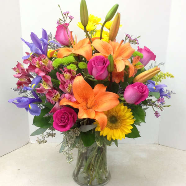 Colorful bouquet of lilies, roses, and a sunflower in a glass vase