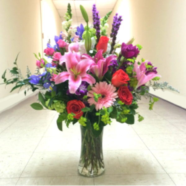 Tall mixed bouquet of pink lilies, roses, and purple flowers in a glass vase