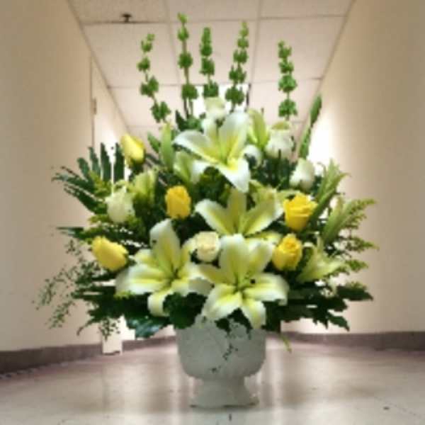 Tall yellow and white lily and rose arrangement in a white urn-style vase