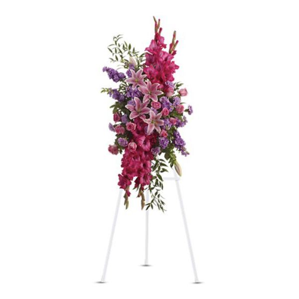 Standing spray of pink lilies, roses, and gladiolus with purple flowers on a white easel