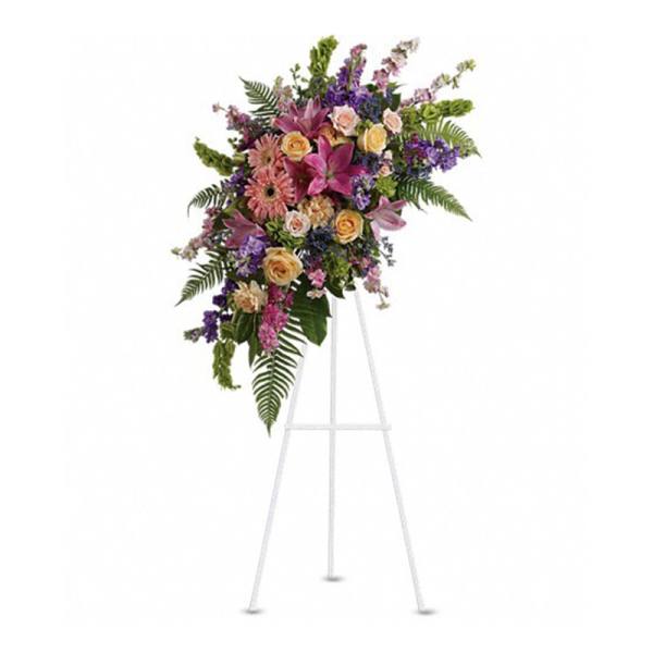Tall standing spray of pink lilies, peach roses, and mixed flowers on a white easel