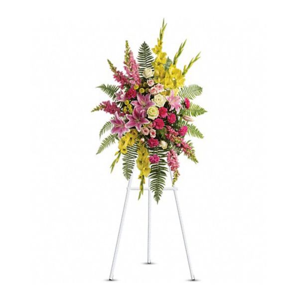 Standing spray of pink lilies, roses, and yellow flowers with ferns on a white easel