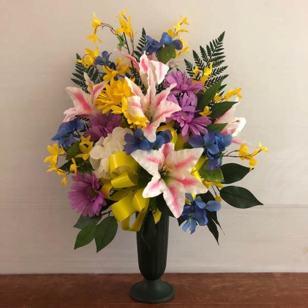Tall arrangement of pink-tipped white lilies with yellow, purple, and blue flowers in a dark vase.