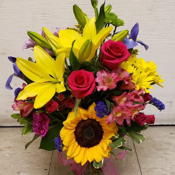Mixed bouquet with yellow lilies, pink roses, and a sunflower in a glass vase