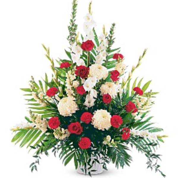 Tall red and white floral sympathy arrangement in a white vase with prominent greenery.