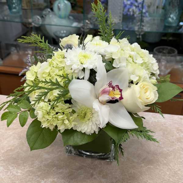 White and pale green floral arrangement in a square glass vase