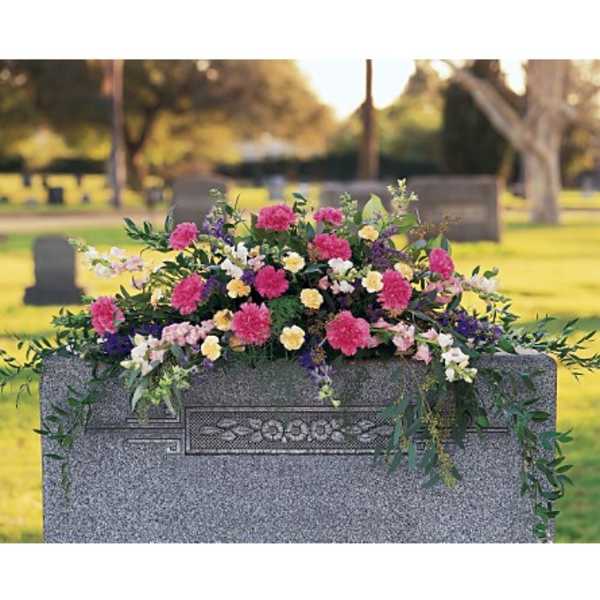 Cemetery saddle arrangement with pink, yellow, and white flowers on a gray headstone