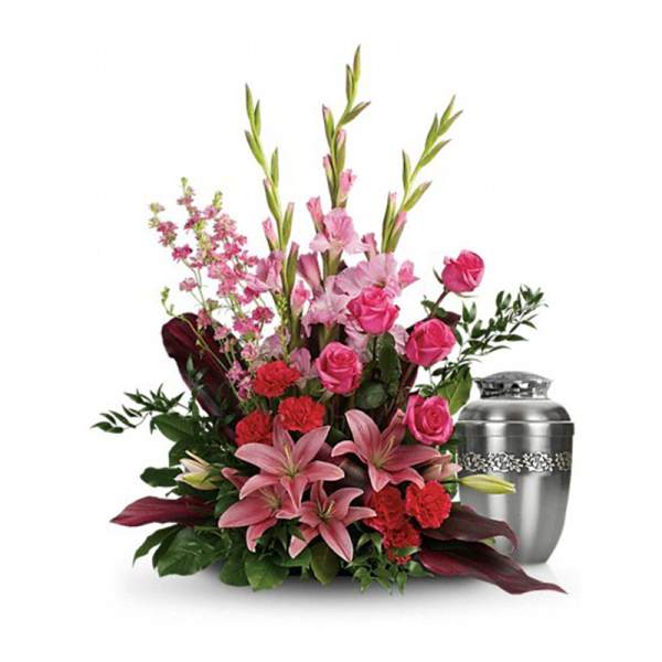 Sympathy floral arrangement of pink lilies, roses, and red carnations beside a silver urn