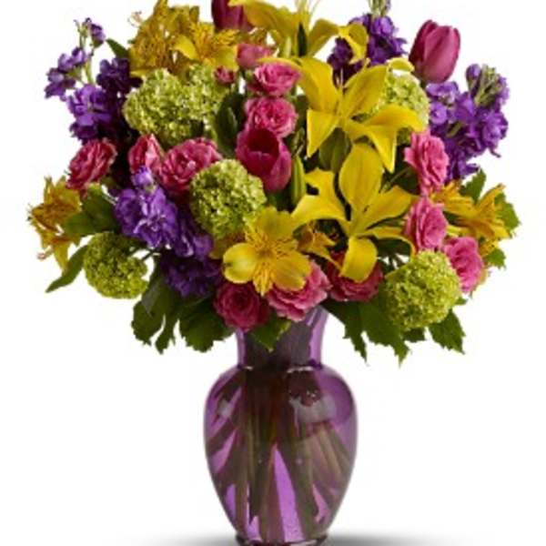 Mixed bouquet of yellow lilies, pink roses, and purple flowers in a purple vase