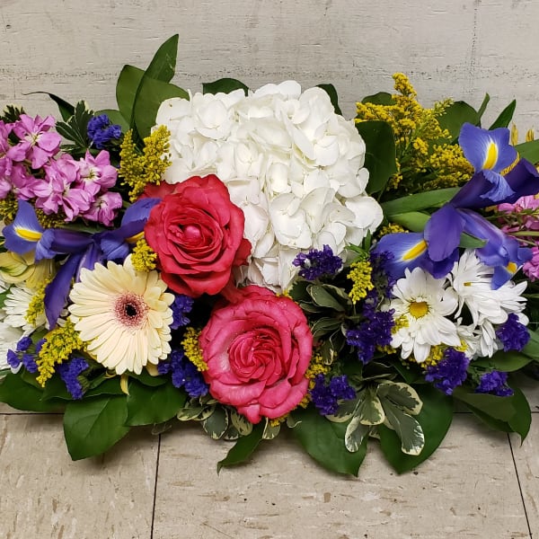Low centerpiece of pink roses, white hydrangea, purple iris, daisies and mixed bright flowers