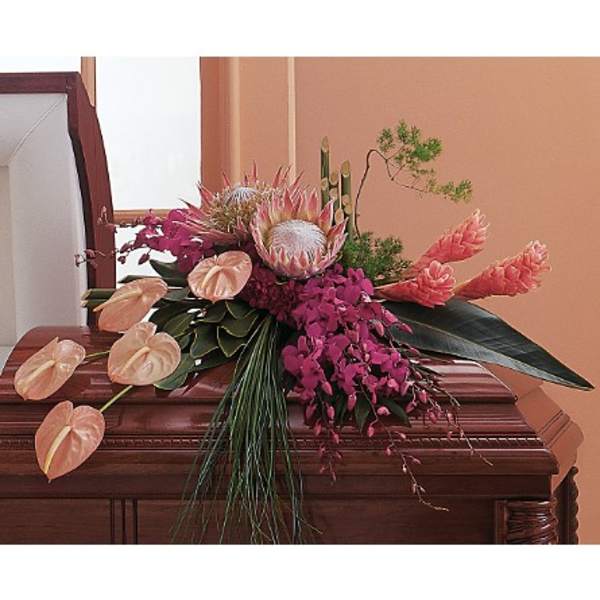 Tropical pink and peach casket spray with protea, orchids, and anthuriums on a wood casket