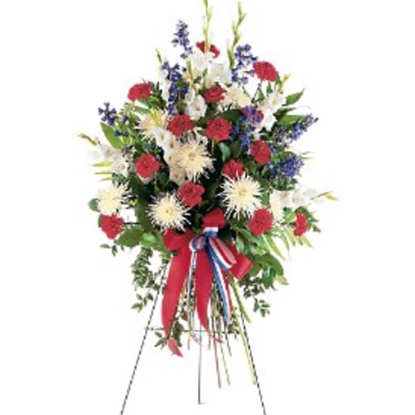Standing spray of red carnations, white mums, and blue flowers on an easel with a patriotic ribbon.