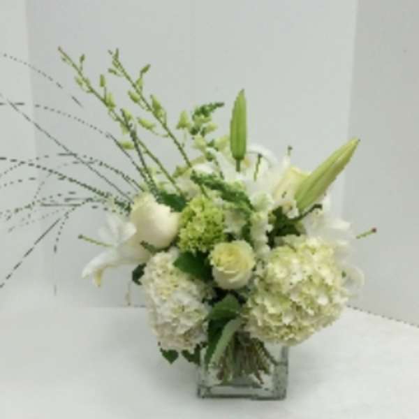 White floral arrangement with lilies and hydrangeas in a square glass vase