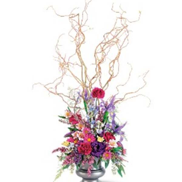 Tall mixed flower arrangement with curly branches in a silver pedestal vase