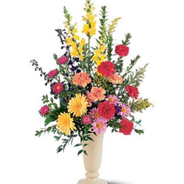 Tall mixed arrangement of bright yellow, red, and pink flowers in a cream pedestal vase