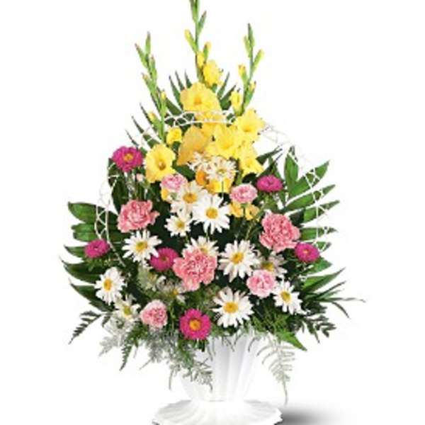 Tall mixed arrangement with yellow flowers, white daisies, and pink blooms in a white pedestal vase