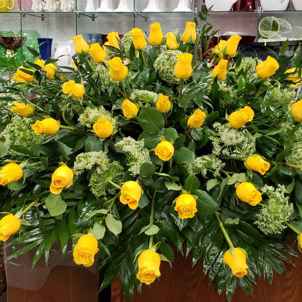 Large horizontal spray of yellow roses with green filler flowers arranged on a wooden base