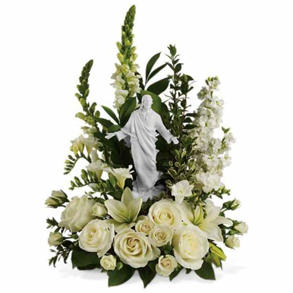 White sympathy arrangement with roses, lilies, and tall blooms surrounding a white Jesus figurine