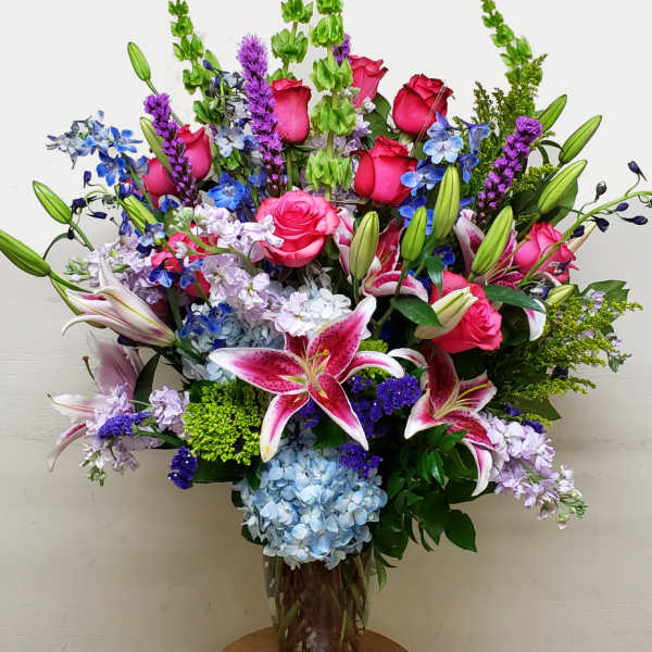 Large mixed bouquet with pink roses, lilies, and blue flowers in a glass vase