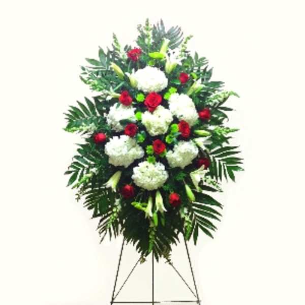 Tall standing funeral spray with white flowers and red roses on a metal easel.