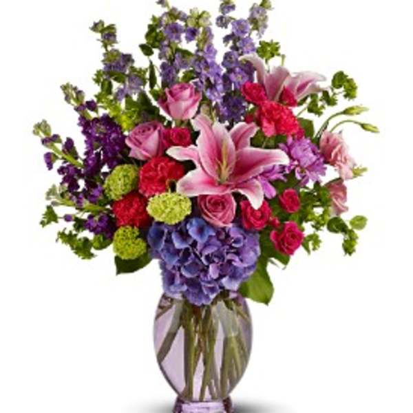 Mixed bouquet with pink lilies, roses, hydrangea, and purple flowers in a glass vase