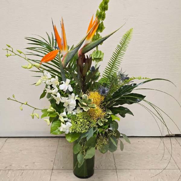 Tall tropical arrangement with orange bird-of-paradise and white orchids in a glass vase