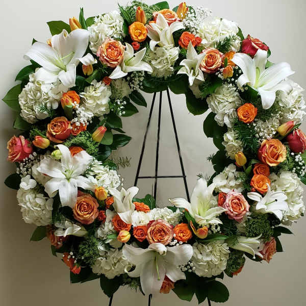 Standing wreath of white lilies, hydrangeas, and orange roses on a metal easel