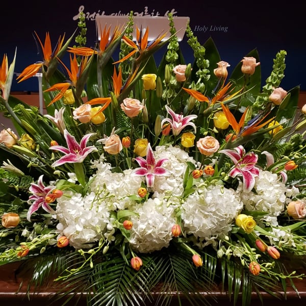 Large altar-style arrangement with white hydrangeas, pink lilies, roses, tulips, and birds of paradise