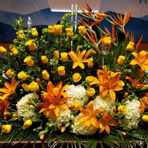 Large altar arrangement of orange lilies, yellow roses, tropical blooms and white hydrangeas.