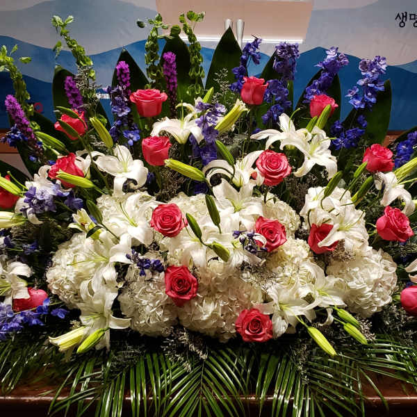 Large altar-style arrangement of white lilies and hydrangeas with red roses and blue delphinium in a fan shape