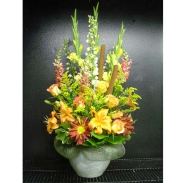 Tall autumn-toned arrangement with orange lilies, roses, and cattails in a frosted vase