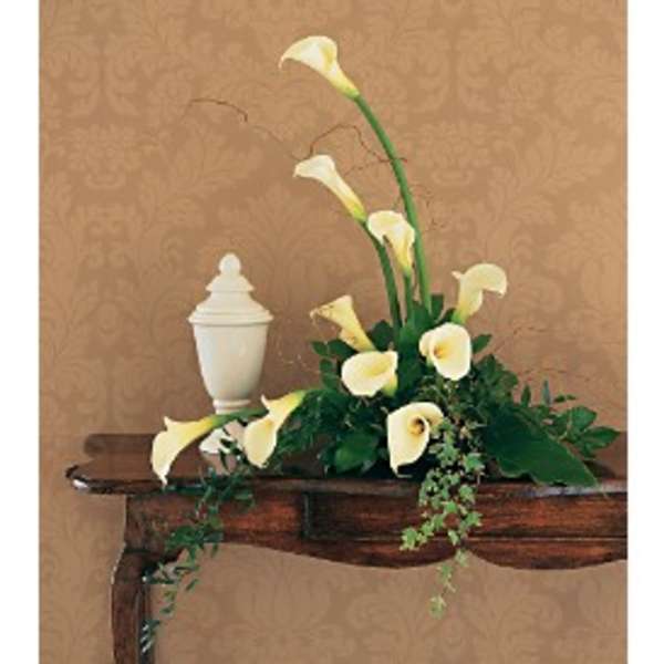 Elegant white calla lily arrangement beside a white urn on a wooden console table