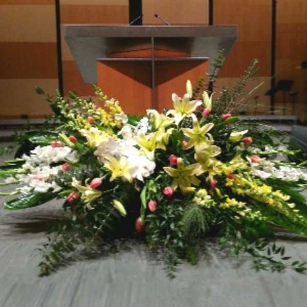 Large altar-style arrangement of yellow lilies, white flowers, and pink buds in front of a podium