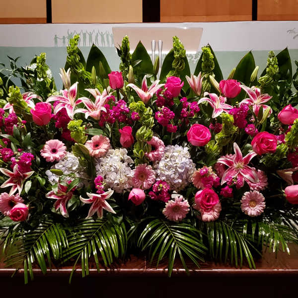 Large pink and white floral stage arrangement with lilies, roses, gerbera daisies, and hydrangeas