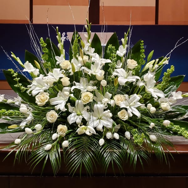 Large white lily and rose arrangement with tulips and Bells of Ireland in a low, fan-shaped design