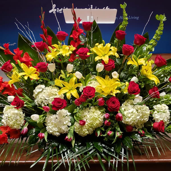Large altar-style arrangement of red roses, yellow lilies, white hydrangeas, and tulips in a fan shape