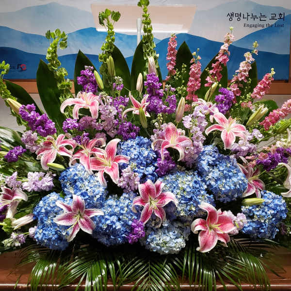 Large floral arrangement with pink lilies, blue hydrangeas, and purple flowers