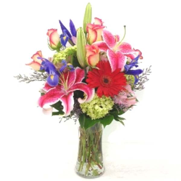 Mixed bouquet of lilies, roses, irises, and a red gerbera in a glass vase