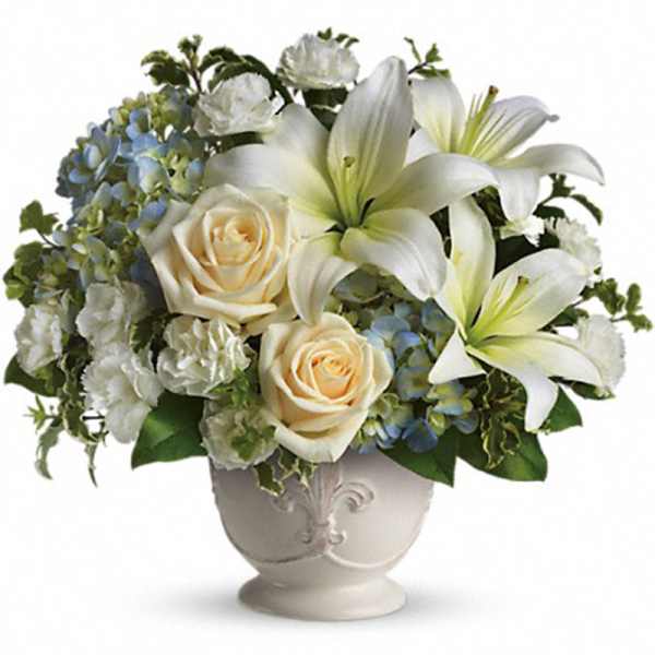 Arrangement of white lilies, cream roses, white carnations and blue hydrangeas in a white footed vase