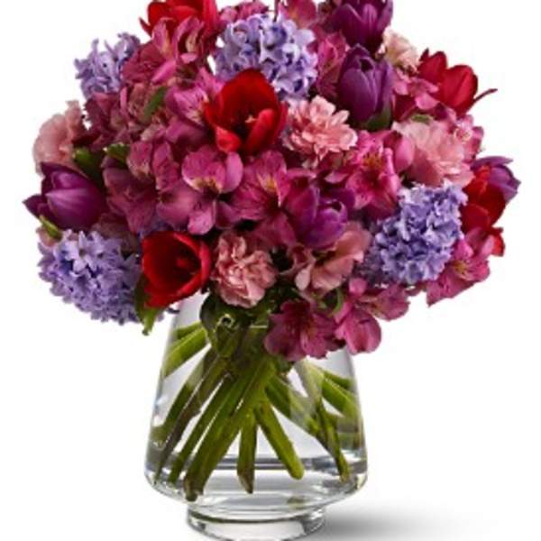 Mixed pink, purple, and red flowers in a clear glass vase