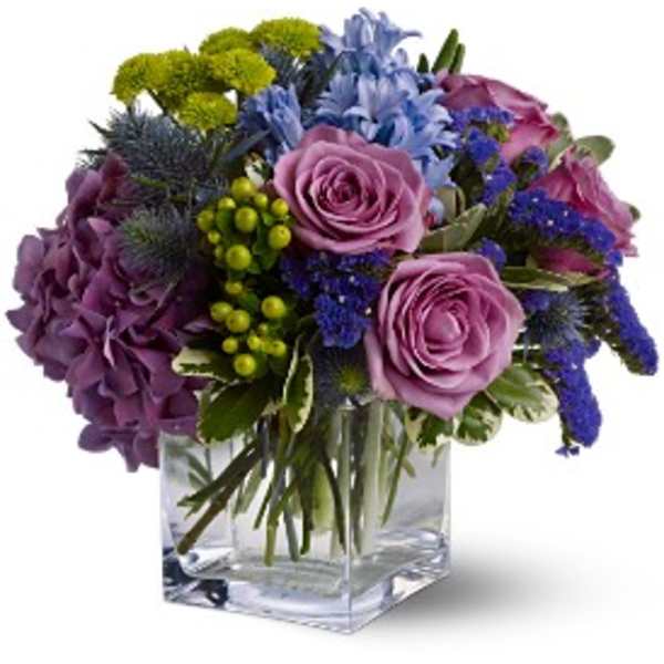 Purple and blue mixed bouquet in a clear square vase