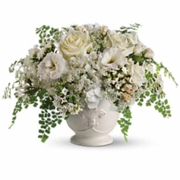 Low white rose and lisianthus arrangement in a white ceramic urn with cascading fern accents