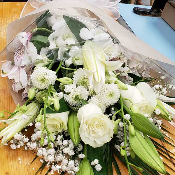 Wrapped bouquet of white roses, lilies, and chrysanthemums with a sheer bow on a wooden table